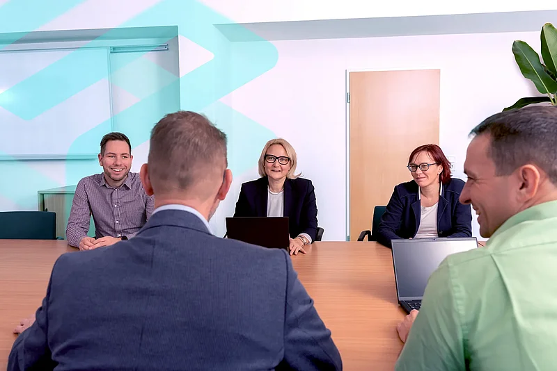 Fünf Mitarbeitende der SAKD sitzen an einem Besprechungstisch und lachen gemeinsam.